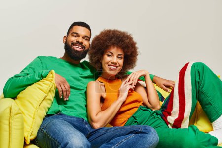 Téléchargez les photos : Heureux amis afro-américains en vêtements vibrants assis sur une chaise de sac de haricot jaune, respirant la chaleur et la proximité. - en image libre de droit