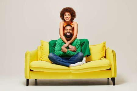 Foto de Felices amigos afroamericanos con ropa vibrante sentados en un sofá amarillo, encarnando la esencia de la amistad entre un hombre y una mujer. - Imagen libre de derechos