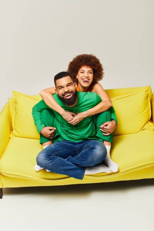Foto de Felices amigos afroamericanos con ropa vibrante se sientan en un sofá amarillo, mostrando la amistad entre un hombre y una mujer. - Imagen libre de derechos