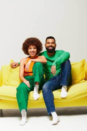 Heureux amis afro-américains en vêtements vibrants assis sur un canapé jaune, mettant en valeur une connexion chaleureuse.