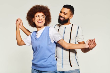 An African American man and woman in stylish clothes dance in sync, showcasing their friendship on a grey background.
