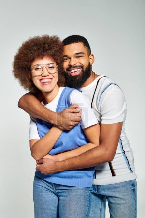 Téléchargez les photos : An African American man and woman in stylish clothes embrace each other, symbolizing friendship and connection on a grey background. - en image libre de droit