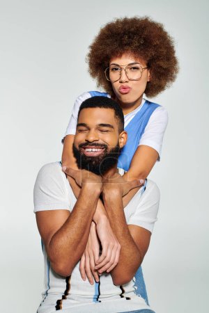 Foto de Hombre y mujer afroamericanos con ropa elegante comparten un momento de corazón mientras la sostiene en sus brazos contra un fondo gris. - Imagen libre de derechos