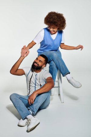 Téléchargez les photos : Un Afro-Américain assis sur une chaise à côté d'une petite fille dans des vêtements élégants, mettant en valeur un moment chaleureux d'amitié. - en image libre de droit