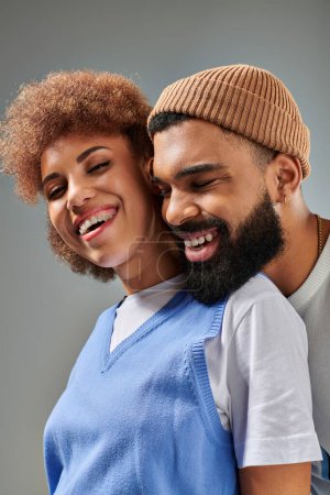 Photo for An African American man and woman in stylish clothes laughing together against a grey background. - Royalty Free Image