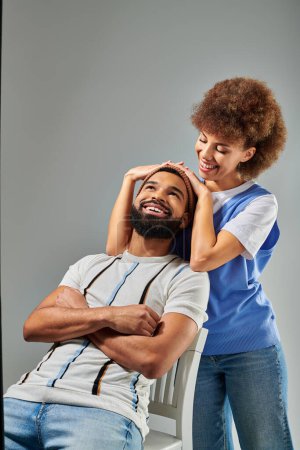 Téléchargez les photos : Un homme et une femme afro-américains en tenue tendance assis sur un banc blanc sur un fond gris. - en image libre de droit