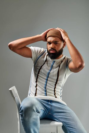 An African American man in stylish clothing sitting on top of a white chair, contemplating with a thoughtful expression.
