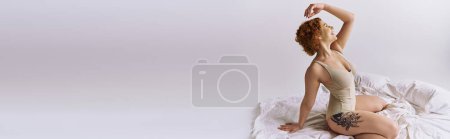 Téléchargez les photos : A young, curvy redhead woman in lingerie striking a pose on a bed against a grey background. - en image libre de droit
