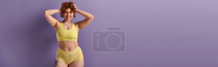 Curvy redhead woman in yellow bikini striking a pose against a vibrant purple backdrop.