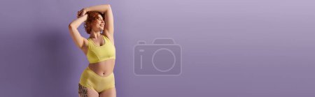 A young and curvy redhead woman exudes confidence as she poses in a yellow bikini against a bold purple background.