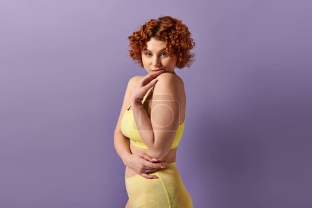 Téléchargez les photos : Curvy redhead in yellow bikini strikes a pose against a vibrant purple backdrop. - en image libre de droit
