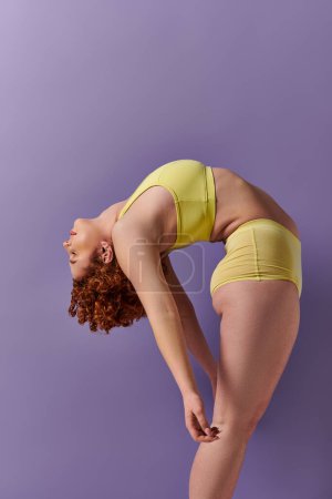 A young, curvy redhead woman in a yellow bikini performs yoga poses on a vibrant purple background.