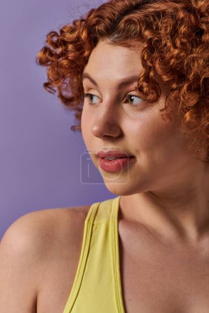 Téléchargez les photos : A young curvy woman with red curly hair poses in front of a purple background. - en image libre de droit