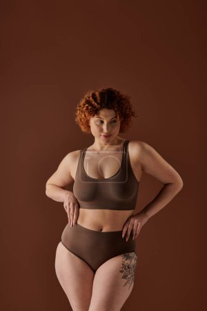 A curvy redhead woman wearing a brown bra and panties, exuding confidence and beauty.