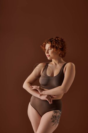 Curvy redhead woman in brown bikini striking a glamorous pose.