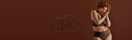Photo for Curvy redhead woman exudes confidence in a stunning bikini on a warm brown backdrop. - Royalty Free Image