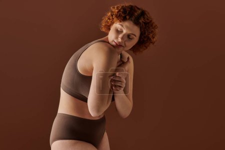 Téléchargez les photos : A young, curvy redhead woman confidently poses in a brown bikini for a captivating shot. - en image libre de droit