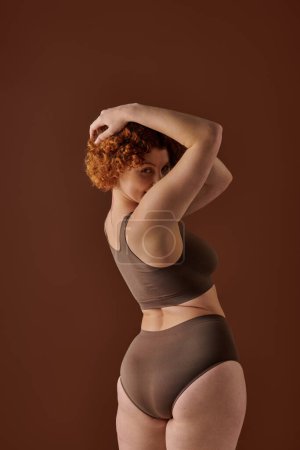 Young, curvy redhead woman in brown bikini striking a pose confidently.