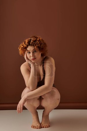 A curvy redhead woman crouching on the floor in her underwear.
