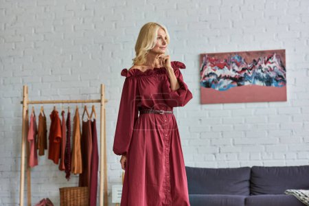 Téléchargez les photos : Une femme mûre dans une robe rouge debout élégamment dans une chambre. - en image libre de droit