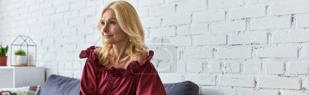Stylish woman in elegant dress sitting on couch in front of brick wall.
