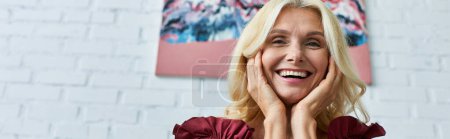 Photo for A mature woman with blonde hair smiles in front of a white brick wall. - Royalty Free Image
