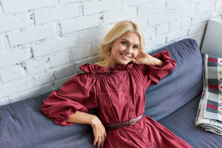 Photo for Stylish woman in red dress on blue couch. - Royalty Free Image