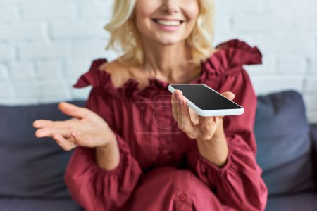 Foto de Mujer madura en traje elegante sentada en el sofá, absorta en el teléfono celular. - Imagen libre de derechos