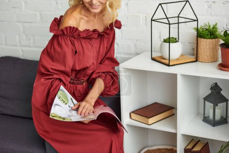 Téléchargez les photos : Femme élégante en robe rouge assise sur un canapé, absorbée dans un magazine. - en image libre de droit