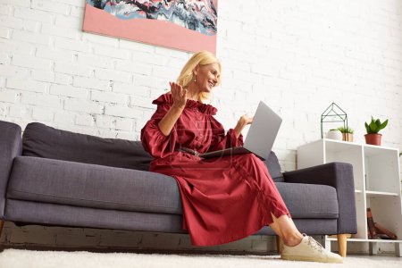 Stylish woman in chic dress sitting on a couch, immersed in laptop use.
