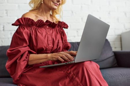 Mujer con estilo en traje elegante sentado en un sofá, absorto en el uso de un ordenador portátil.