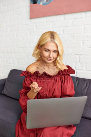 Foto de Una mujer sofisticada con un atuendo elegante, absorta en su computadora portátil en el sofá. - Imagen libre de derechos