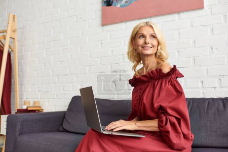 Una mujer sofisticada con un vestido elegante se sienta en un sofá usando una computadora portátil.