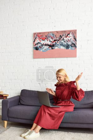 Stilvolle Frau im schicken Kleid mit einem Laptop auf einer bequemen Couch.