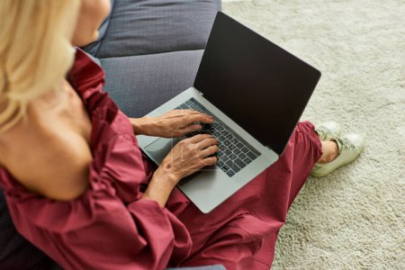 Una mujer con estilo absorto en su ordenador portátil mientras está sentado en un sofá en casa.