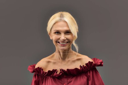 Une femme mature et élégante aux cheveux blonds dans un chemisier rouge, respirant la confiance et le style.