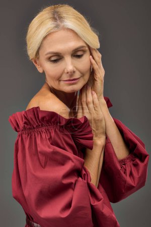 Mature woman in red dress in a moment of contemplation, hands raised to face.