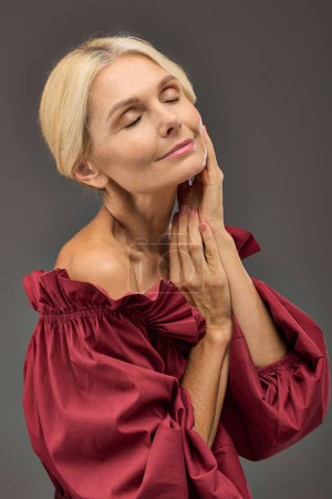 Elegant lady in a red top, deep in thought, hand resting on face.
