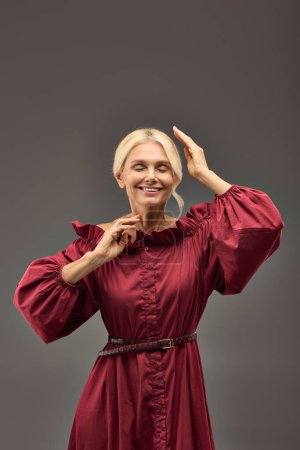 A mature elegant woman in a red chic dress striking a pose.