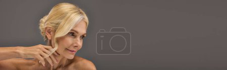 Blonde woman poses gracefully against gray backdrop.