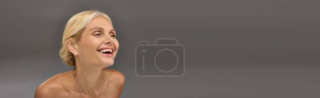 Eine reife Frau mit einem Lächeln vor grauem Hintergrund.