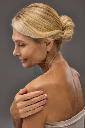 Téléchargez les photos : Heureuse femme mature avec des cheveux blonds posant sur fond gris. - en image libre de droit