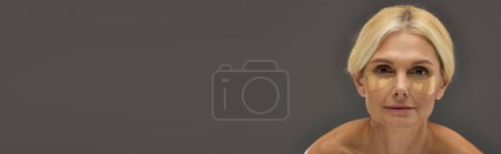 Foto de Hermosa mujer madura con cabello rubio con parches en los ojos sobre un fondo gris. - Imagen libre de derechos