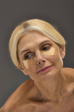 Attractive mature woman with blonde hair with eye patches on a gray backdrop.
