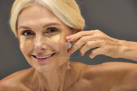 Reife Frau zeigt Augenklappen bei der Hautpflege.