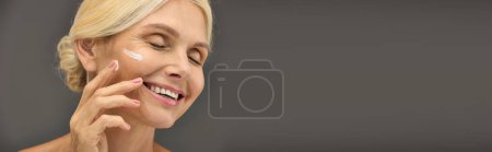 Photo for Beautiful mature woman with cream on face poses against a grey backdrop. - Royalty Free Image