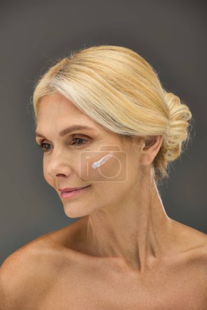 Mature woman showcasing her skincare routine with cream on face.