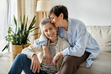 Two elderly women sharing a warm hug on a couch.