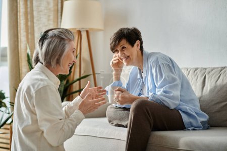 Two elderly women engaged in lively conversation on a cozy couch.