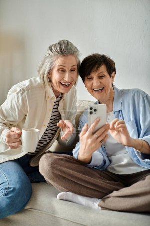 Photo for Two women engage with their phones while seated on a cozy couch. - Royalty Free Image